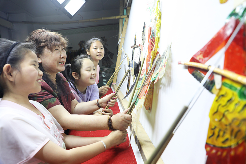 皮影藝人指導小朋友表演皮影戲。